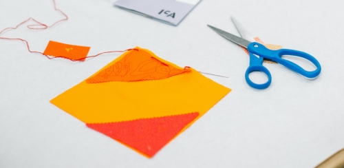 A piece of orange fabric square next to a pair of scissors on a table.