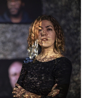 Photo of artist Rashin Fahandej in front of her artwork consisting of photographs of men.