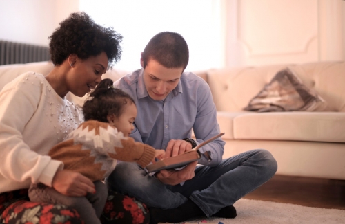 Family sitting on floor while reading book.