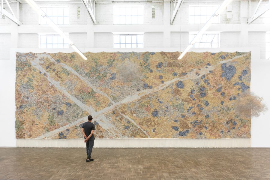 Person standing in front of large woven artwork on wall