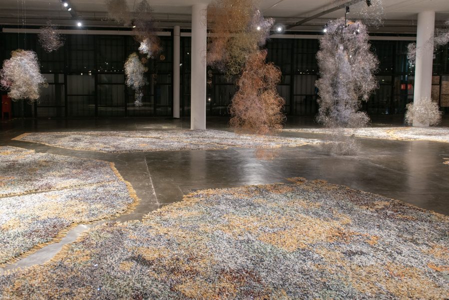 woven artwork on the floor with clouds made of metal material hanging from ceiling