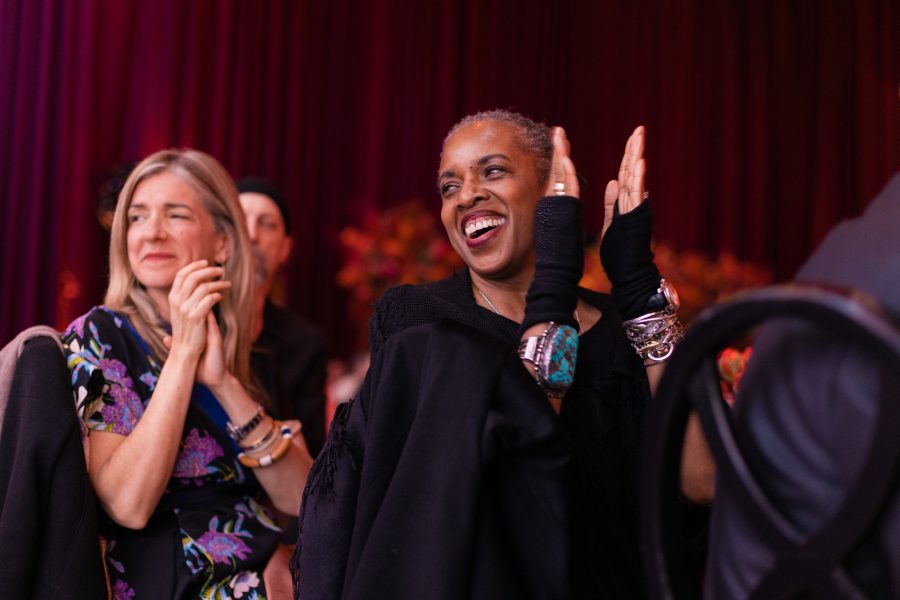 A middle-aged Black woman and a middle-aged blond light-skinned woman smile and clap at an event.